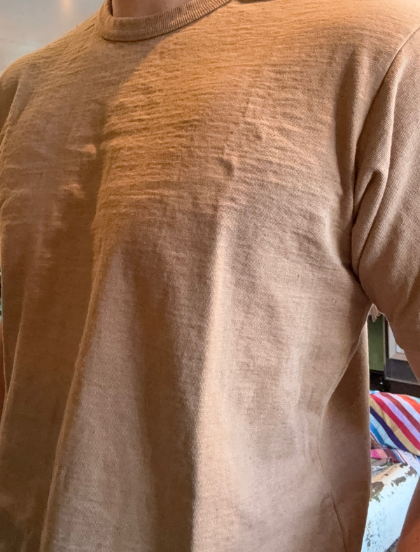 A close-up of a person wearing a short-sleeve crewneck t-shirt in a warm tan or light brown color.