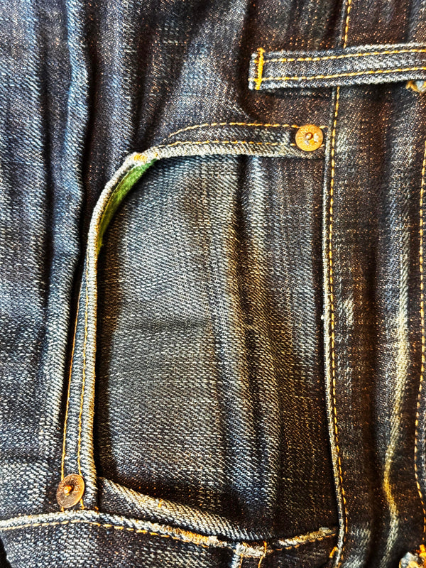 Close-up of a dark indigo denim pocket with contrast yellow stitching and brass-toned rivets.