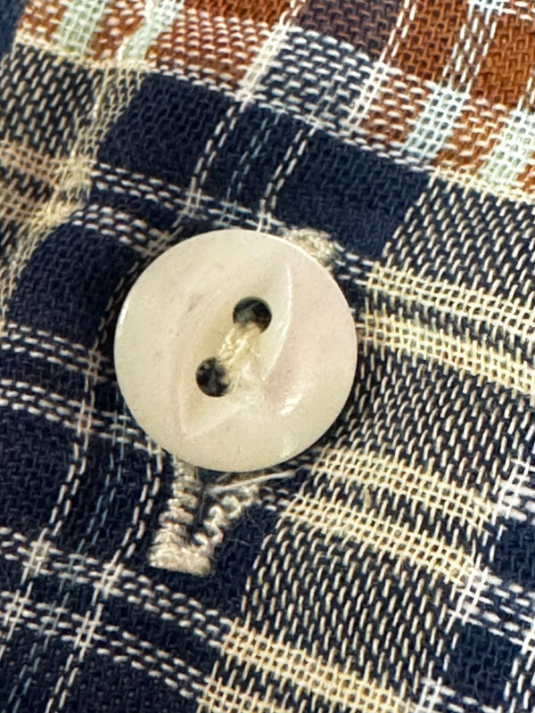 A close-up of a single round white button with two holes, placed on a navy, beige, and brown plaid fabric background.