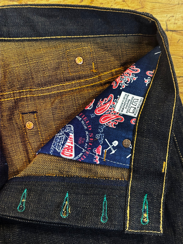Close-up of a pair of dark indigo denim jeans showing the inner waistband, yellow contrast stitching, and a patterned inner lining with a visible sewn-in label.