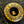 A close-up of a round brass button with an engraved laurel wreath and star pattern, set against a black textured fabric background with yellow stitching.