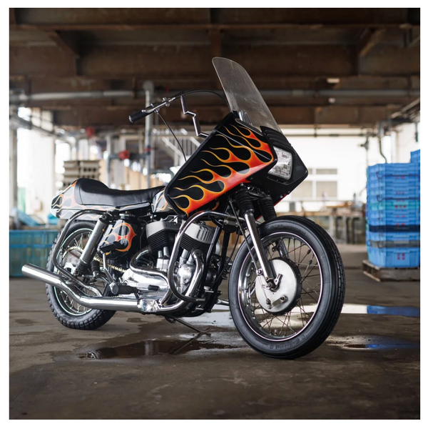 A black motorcycle with orange and yellow flame decals on the fuel tank, parked in a warehouse setting.