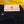 Close-up of the waistband of black denim jeans with a white and red 'Left Field' brand label, placed on a yellow wooden floor.