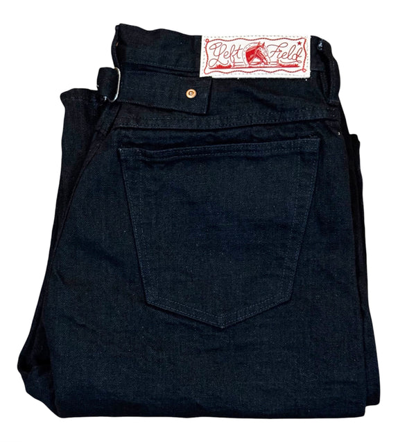 A pair of folded dark indigo denim jeans with a white and red 'Left Field' brand patch visible at the waistband, set against a plain white background.