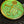A close-up of a round, antique-style metal button or medallion with a green patina and gold-toned lettering and symbols, resting on a dark textured fabric background.
