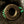 Close-up of a round bronze-toned metal button with engraved leaf and star motifs, set into dark textured fabric with bright green thread accents.
