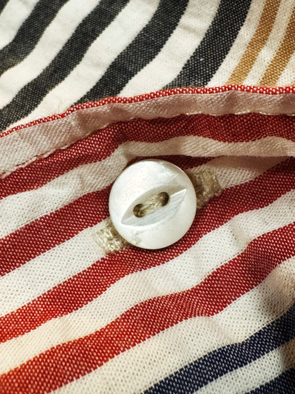 A close-up of a white button sewn onto striped fabric with red, navy, black, and beige horizontal bands.