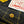 Close-up of dark indigo denim fabric with yellow contrast stitching, a wooden button, and a white sewn label printed with red script reading 